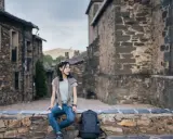 Junge Frau sitzt auf Steinmauer in historischem Dorf in Guadalajara, Spanien.