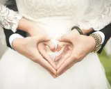 Manos formando un corazón, celebrando 2 años de casados. Vestido de novia blanco y traje negro.