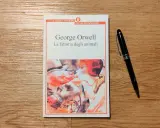 Copertina del libro "La fattoria degli animali" di George Orwell, con una penna nera appoggiata accanto.