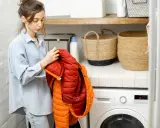 Mujer revisa un anorak naranja y rojo, preparándose para saber como lavar un anorak en la lavadora.