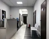 Korytarz kliniki medycznej z recepcją, drzwiami i białymi krzesłami.