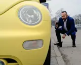 Rzeczoznawca samochodowy w garniturze klęczy przy żółtym samochodzie, robiąc zdjęcie aparatem.