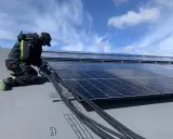 Installatör arbetar med solpaneler, drar kablar. Olika batteri storlekar kan behövas för att optimera energilagringen.