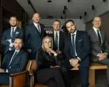 Grupa siedmiu profesjonalistów w garniturach, pozujących do zdjęcia w biurze.