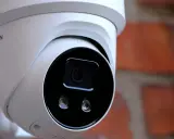 Vit övervakningskamera med Hikvision-logotyp, monterad mot en tegelvägg. Ger trygghet med larmklass 1.