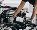 Mechanik w rękawiczkach pracuje przy silniku, dbając o zgodność z normami emisji spalin i tabelą CO2.