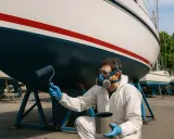 Homme en combinaison et masque appliquant l'antifouling bateau sur remorque avec un rouleau.