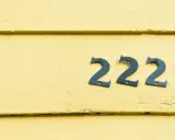 Niebieskie cyfry 222 na żółtej, drewnianej ścianie. Liczba 222 ma dla mnie szczególne znaczenie.