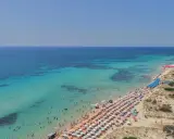 Un tratto di costa con acque cristalline e sabbia dorata, tra le spiaggie più belle del Salento, affollata di ombrelloni e bagnanti.