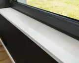 Biały, lśniący parapet z konglomeratu, idealnie wypolerowany, stanowi eleganckie wykończenie okna.