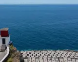 Kleines rotes Haus auf Felsen am Meer bei Ribeira Brava. Wellenbrecher aus Beton säumen die Küste.