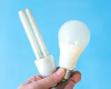 Une ampoule fluocompacte et une ampoule LED sont tenues dans une main, illustrant la puissance LED moderne.