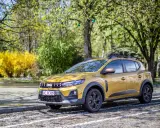 Złoty Dacia Sandero Stepway na tle wiosennej zieleni i kwitnącego krzewu.
