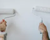 Dwie osoby malują ścianę wałkami. Wybór między farbą lateksową a akrylową zależy od efektu.