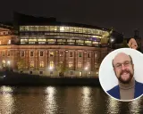En man ler mot kameran framför Riksdagshuset i Stockholm, en symbol för representativ demokrati.