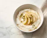 Cremiger Joghurt, der zu lange im Joghurtbereiter war, serviert mit Birnenspalten, Honig und gehackten Pistazien.