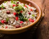 Salade de riz gastronomique, un plat coloré avec des grains de grenade, des cacahuètes et de la coriandre fraîche dans un bol en bois.