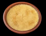 Crème brûlée dans un ramequin en terre cuite, sa surface caramélisée craque sous la cuillère.