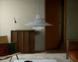 En ikonisk PH-lampa från Poul Henningsen hänger över ett vardagsrum med en läderfåtölj och en träbyrå.