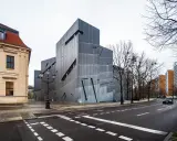 Nowoczesny budynek Muzeum Żydowskiego w Berlinie, obok zabytkowej kamienicy, z charakterystyczną, poszarpaną fasadą.