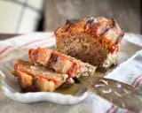 Un délicieux pain de viande, garni de tomates et de lardons, est servi sur une assiette blanche.