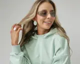 Uśmiechnięta blondynka w miętowej bluzie i okularach przeciwsłonecznych, prezentująca swój modny styl.
