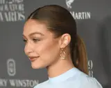 Gigi Hadid mit glatten, **haare nach hinten** gebundenen Haaren und einem dezenten Lächeln. Sie trägt ein hellblaues Oberteil und auffällige Ohrringe.