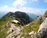 Sentiero panoramico verso il rifugio Lecco, con escursionisti su un crinale erboso e roccioso sotto un cielo azzurro.