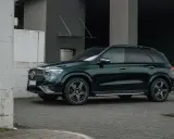 Ciemnozielony Mercedes GLE AMG stoi przed nowoczesnym budynkiem.
