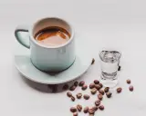 Kawa i alkohol skutki: filiżanka espresso obok kieliszka z wodą i rozsypane ziarna kawy.