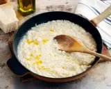 Krämig risotto i panna med en träsked. Bredvid syns parmesanost, olivolja och en rivare. Frågan är om man kan frysa risotto?
