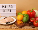 Na stole świeży kurczak, warzywa i owoce. Tablica z napisem "PALEO DIET" sugeruje zdrowe odżywianie.