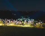 Ciclisti nella notte, illuminati da laser che formano il logo "Pedala coi Lupi". Un'avventura notturna su due ruote.