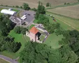 Chudów atrakcje: ruiny zamku z czerwoną wieżą, biały namiot, budynek z drewnianym dachem i parking.