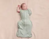Un neonato dorme sereno, avvolto in una fascia che lo culla dolcemente.
