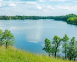 Malownicze żnin jezioro otoczone zielenią, z widocznymi domami na horyzoncie i błękitnym niebem z chmurami.