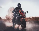 Motocyklista w kasku i kombinezonie na sportowym motocyklu, otoczony dymem. Czy motorem można jeździć po autostradzie? Tak, jeśli spełnia określone wymogi.