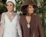 La madre de la novia, elegante con sombrero marrón, acompaña a la radiante novia con su vestido blanco adornado.