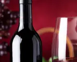 Bouteille de vin rouge connu, verre à vin et grappe de raisins sur fond rouge.
