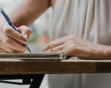 Dłoń pisze długopisem w notatniku, ucząc się, jak napisać artykuł.