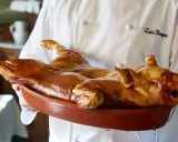 Cochinillo asado, un clásico que comer en Segovia. Un chef presenta este manjar dorado en una cazuela.