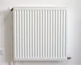 Radiador blanco con termostato, junto a un enchufe. Podría estar haciendo ruido radiador.