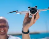 Ręka trzyma drona DJI Mini 3 Pro, gotowego do lotu. Jego imponujący zasięg pozwoli na uchwycenie niesamowitych ujęć.