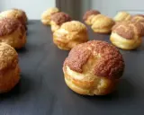 Une rangée de choux craquelins dorés et croustillants, certains avec un dessus brun, prêts à être dégustés.