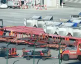Röda lastbilar och vagnar med bagage på en solig yta vid teneriffa flygplats. En gaffeltruck står redo.