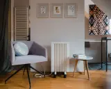 Un fauteuil confortable, un radiateur rayonnant blanc et une petite table avec des livres créent un coin lecture cosy.