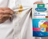 Biała koszula z brązowymi plamami i opakowanie odplamiacza Dr. Beckmann.