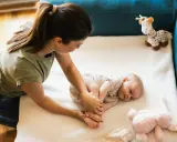 Mama bawi się z 3 miesięcznym dzieckiem, delikatnie masując jego stópki. Obok leżą pluszowe zabawki.