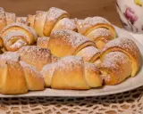 Talerz pełen puszystych, posypanych cukrem pudrem rogalików krucho drożdżowych. Idealne na śniadanie lub deser.
