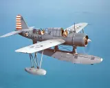 Ein Wasserflugzeug mit zwei Piloten fliegt über das Meer. Die Markierungen auf dem Flugzeug sind die von siai Marchetti.